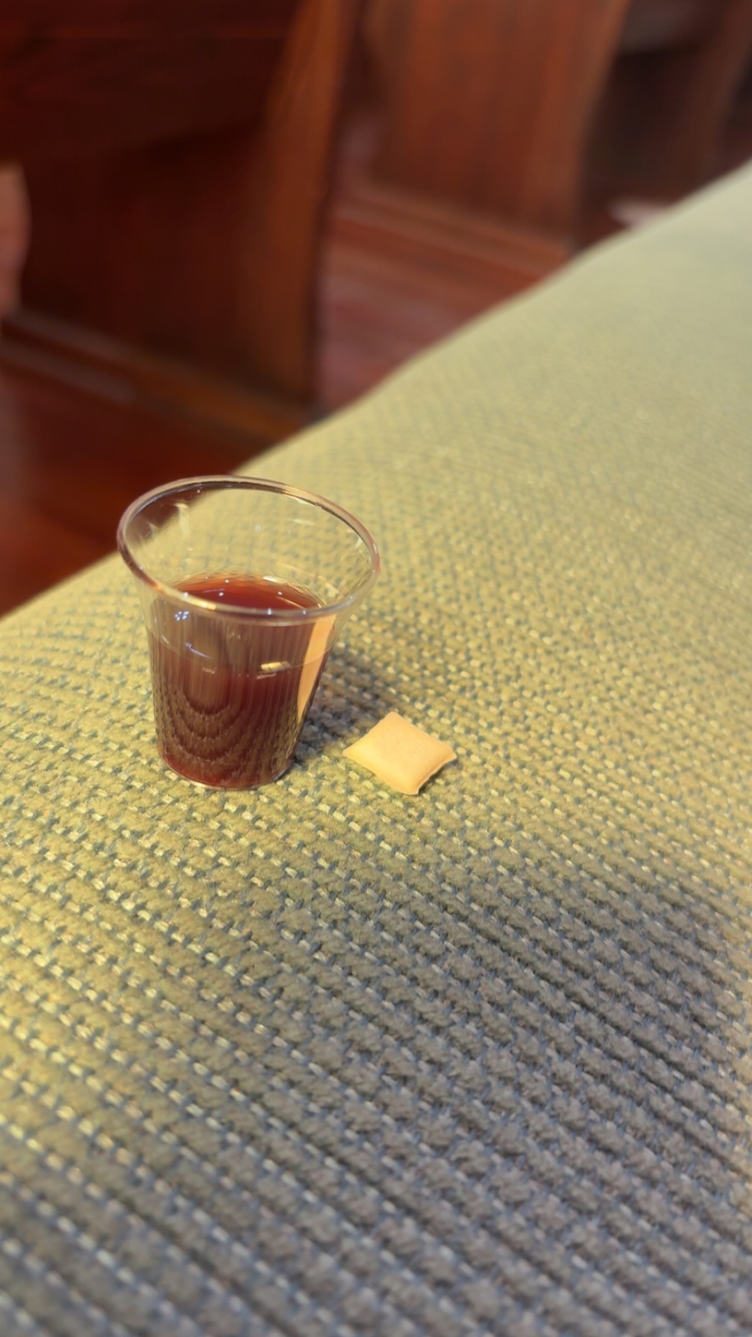Communion cup of juice and a sealed wafer resting on the pew
